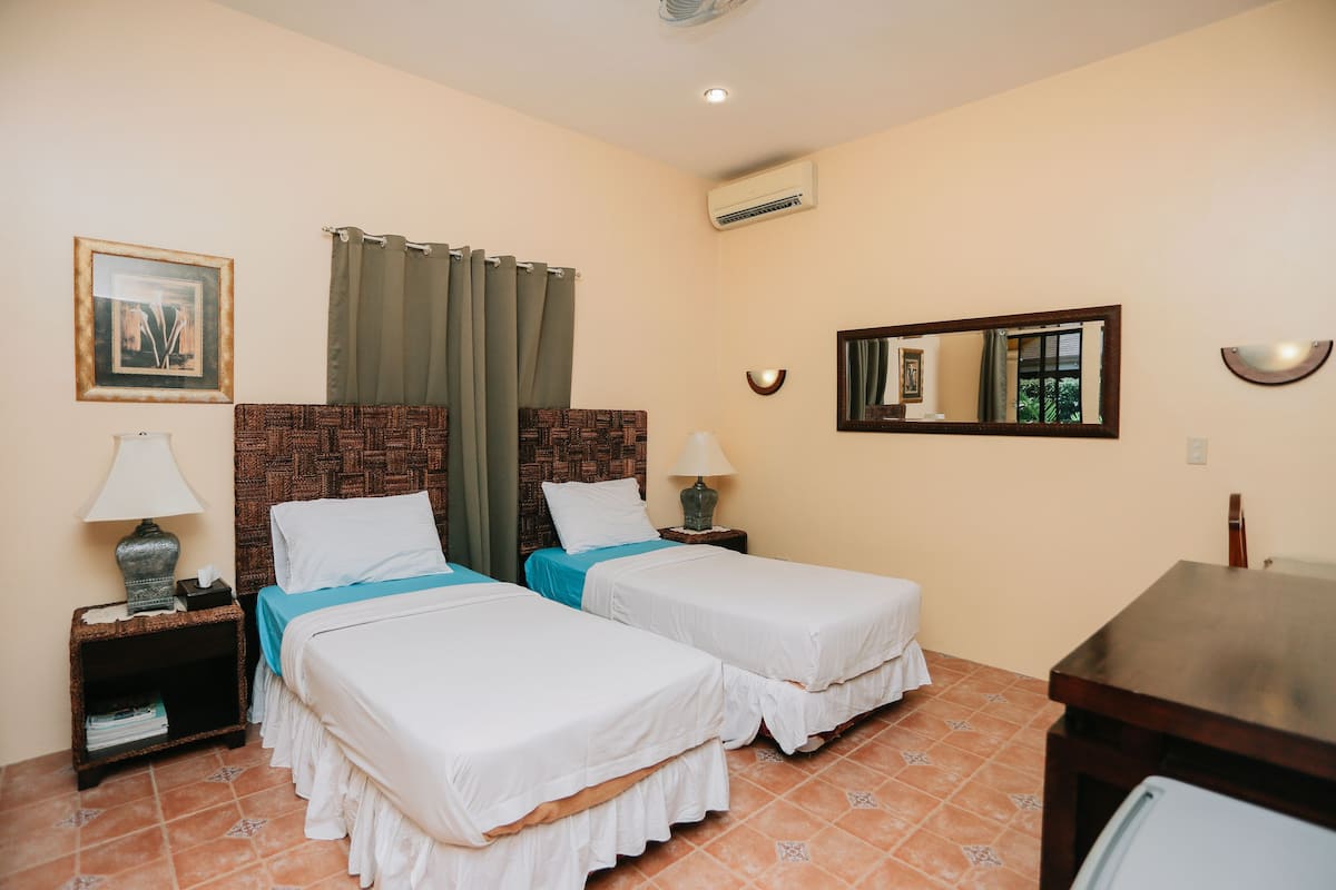 A hotel room with two single beds, a nightstand with a lamp, a small table, and a mirror.