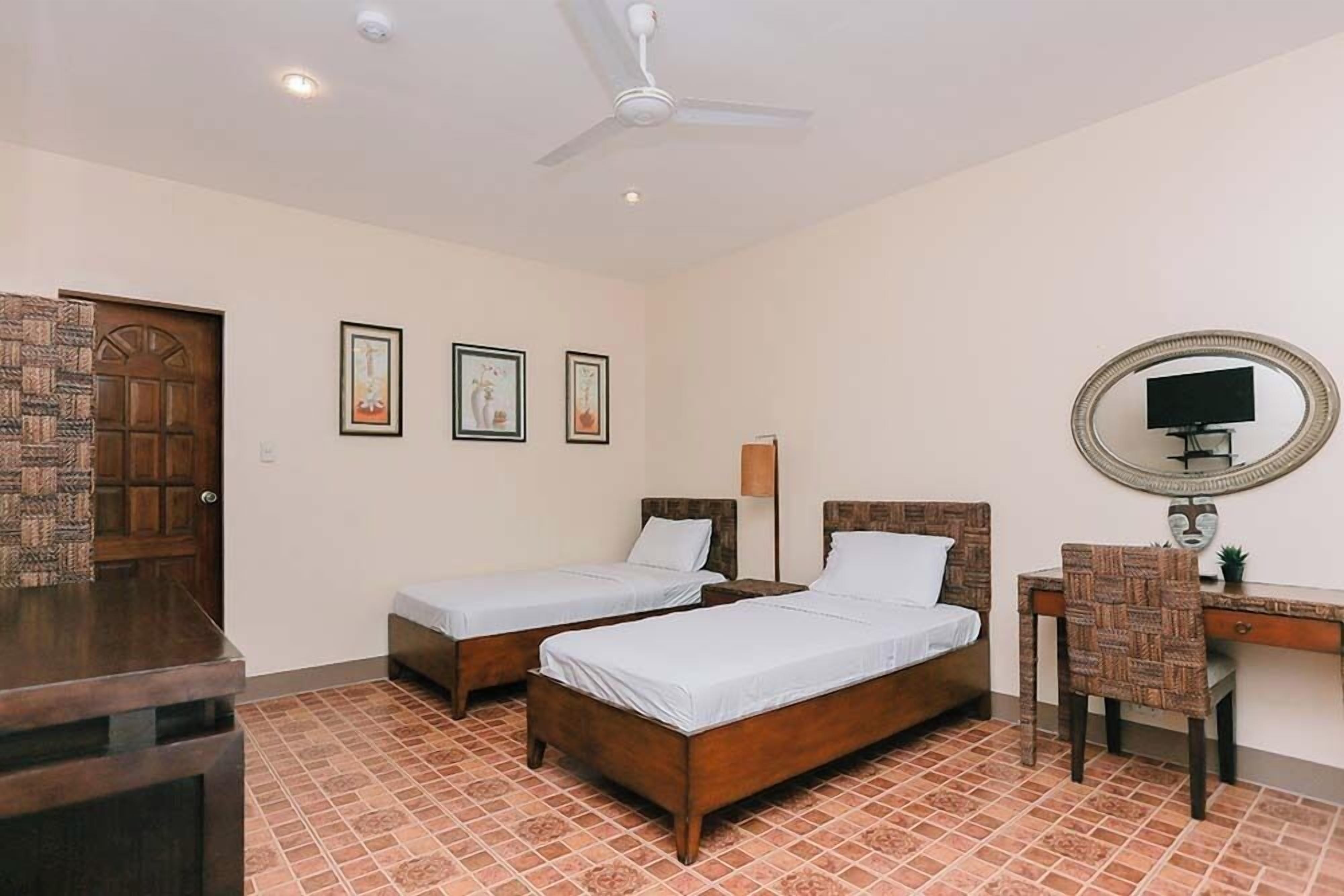 A room with two wooden beds, a desk with a chair, a mirror, and a door.