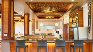 Zona de bar con techo de madera, taburetes y una barra llena de botellas.