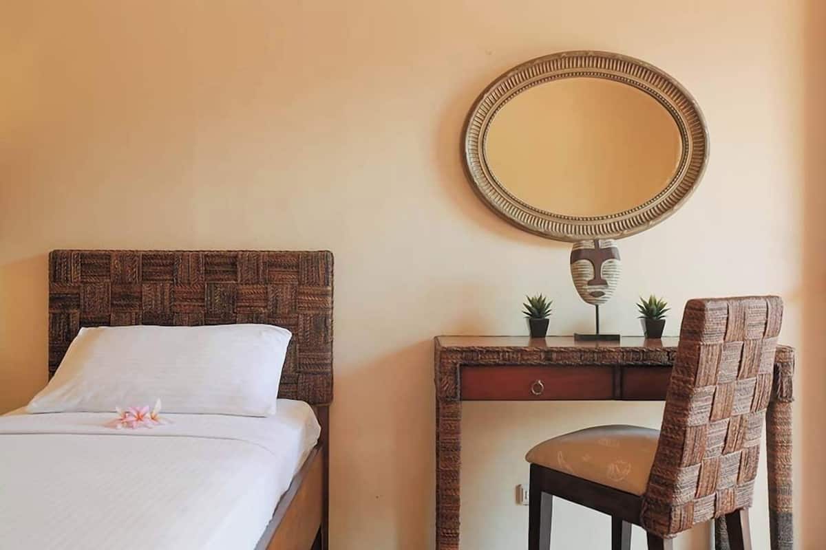 A bed with a woven headboard, a bedside table with a mirror, a chair, and a small plant on the table.