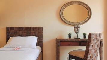 A bed with a woven headboard, a bedside table with a mirror, a chair, and a small plant on the table.