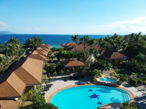 A resort with a swimming pool, palm trees, and a view of the ocean. - Turtle Bay Dive Resort (Moalboal)