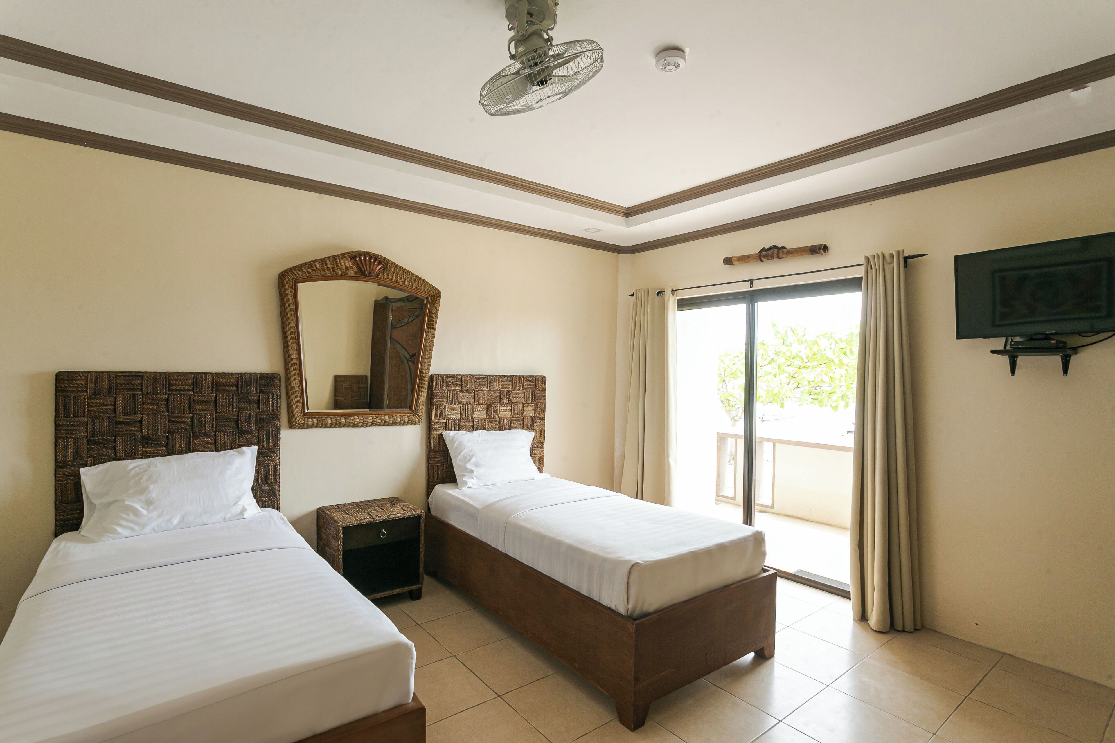 A hotel room with two single beds, a large mirror, a ceiling fan, a television, and a sliding glass door to the outside.