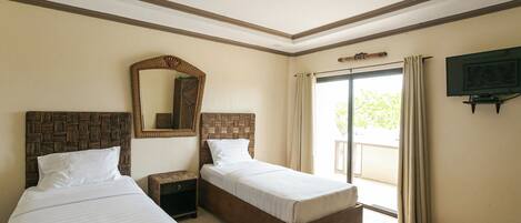 A hotel room with two single beds, a large mirror, a ceiling fan, a television, and a sliding glass door to the outside.