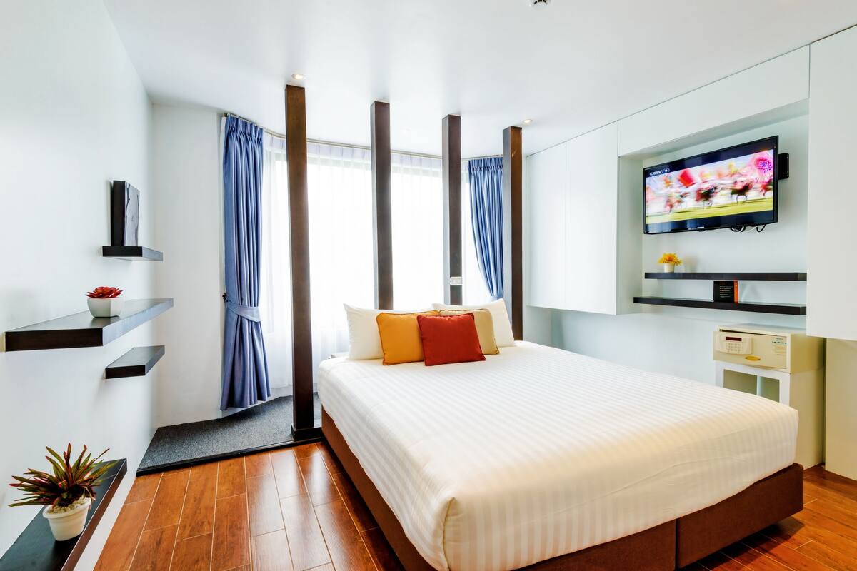 A modern hotel room with a large bed, a TV mounted on the wall, and a small bedside table.