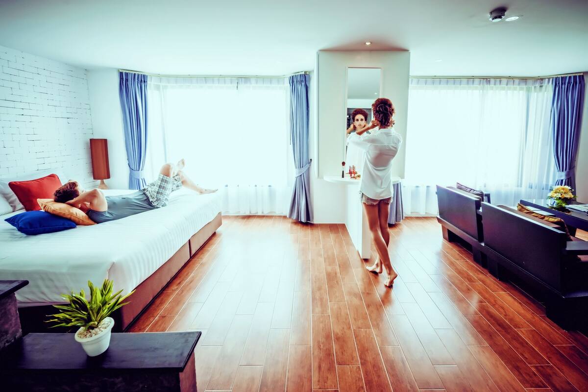 A modern hotel room with a bed, a sitting area, a TV, and a bathroom.
