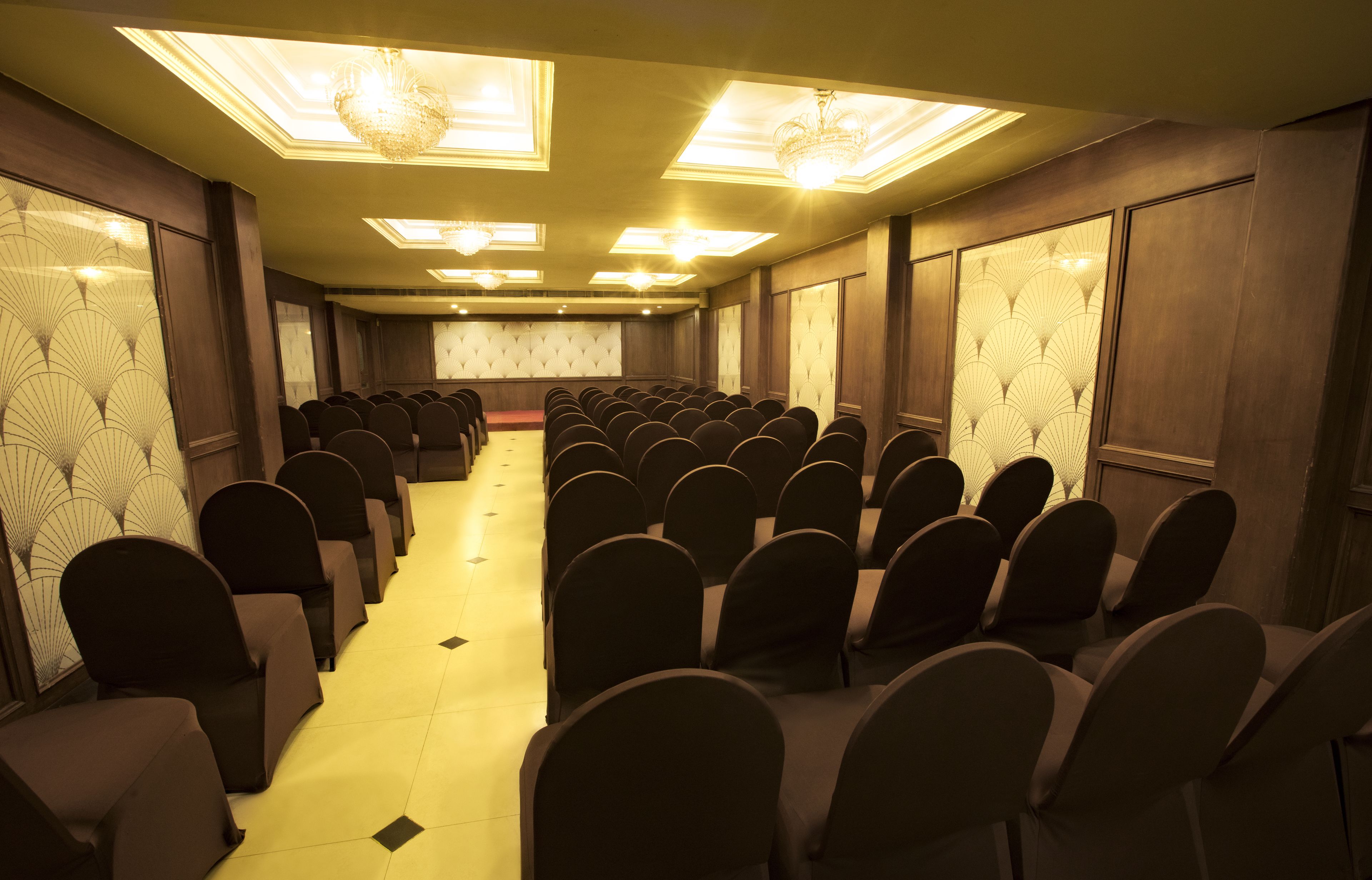 Une salle de conférence avec des rangées de chaises, une scène et un lustre.