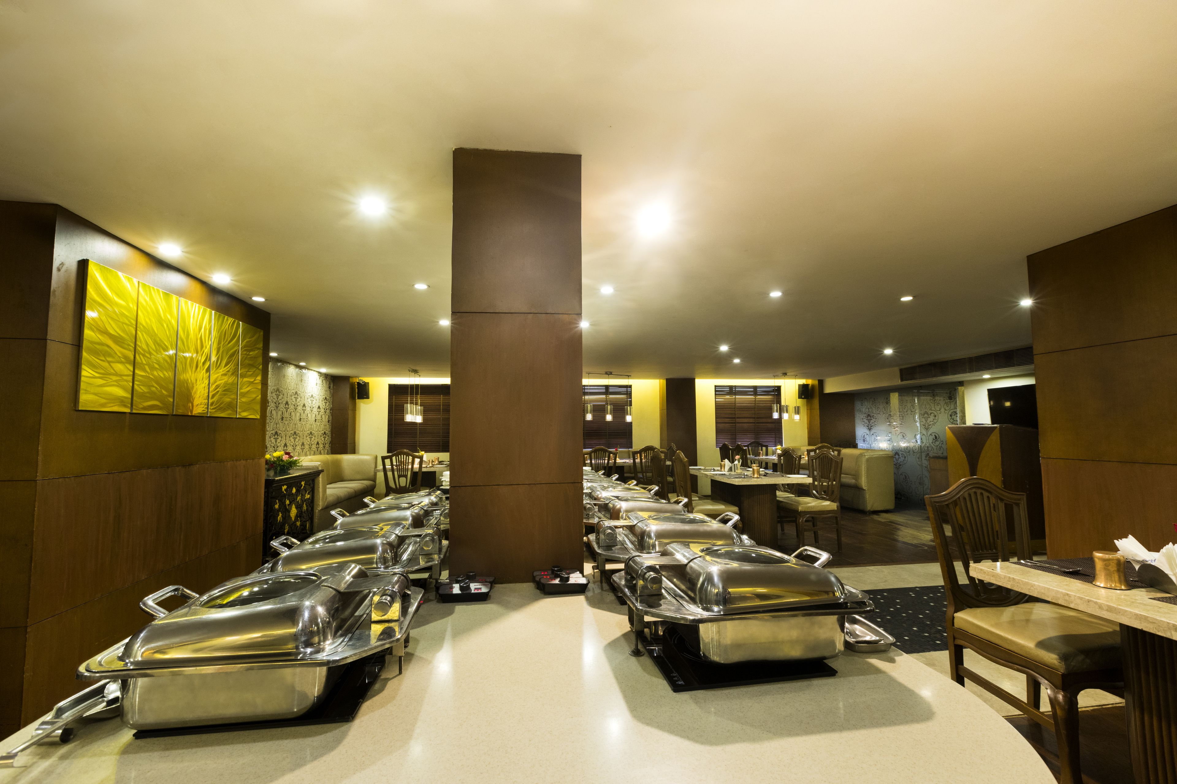 A buffet setup with multiple serving stations, a central pillar, and a dining area with tables and chairs.