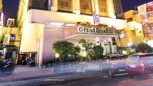 Un hotel alto con una entrada imponente, ventanas grandes y un cartel que dice 'Grand Residence'.