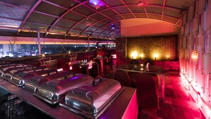 Un restaurante con terraza cubierta, mesas, sillas y vistas de la ciudad por la noche.