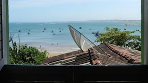A view from a window overlooking a beach with boats on the water and a satellite dish on the roof. - Pousada Caravelas (Guarapari)