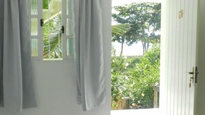 A room with a white door and window, curtains, and a view of greenery outside. - Pousada Caravelas (Guarapari)