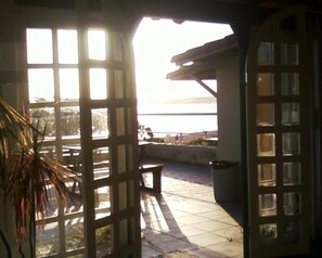 Vista a través de una ventana con diseño de cuadrícula, que da a un patio con una banca y vista a una masa de agua.