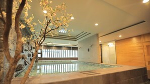 A modern indoor pool area with stone walls, a wooden cabinet, and a tree with blossoms. - OHYA Chain Boutique Motel-Linkou (New Taipei City)
