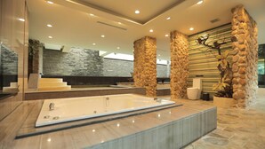 A modern bathroom with a large bathtub, stone pillars, and a stone wall with a tree branch decoration. - OHYA Chain Boutique Motel-Linkou (New Taipei City)
