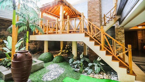 A modern interior with a wooden staircase, a thatched-roof structure, and lush indoor plants. - OHYA Chain Boutique Motel-Linkou (New Taipei City)