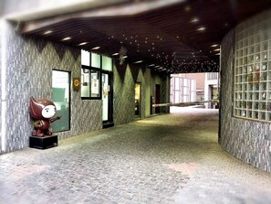 A covered walkway with stone walls and a tiled floor, leading to a building entrance. - OHYA Chain Boutique Motel-Linkou (New Taipei City)