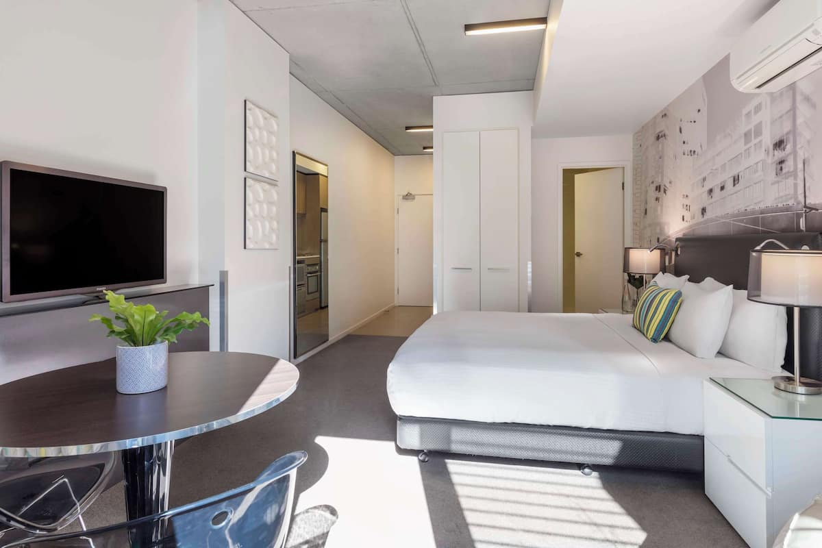 A modern hotel room with a bed, bedside table, lamp, TV, and a small potted plant.