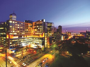 A multi-story hotel with a modern architectural design, featuring a prominent corner building with a glass facade and illuminated windows. - Oaks Melbourne on William Suites (Melbourne)