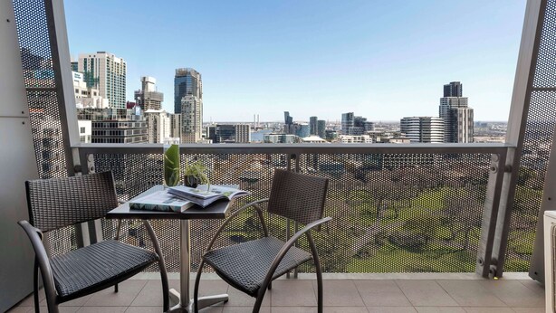 Un balcon offrant une vue sur les gratte-ciel d’une ville, avec des bâtiments modernes et un ciel dégagé.