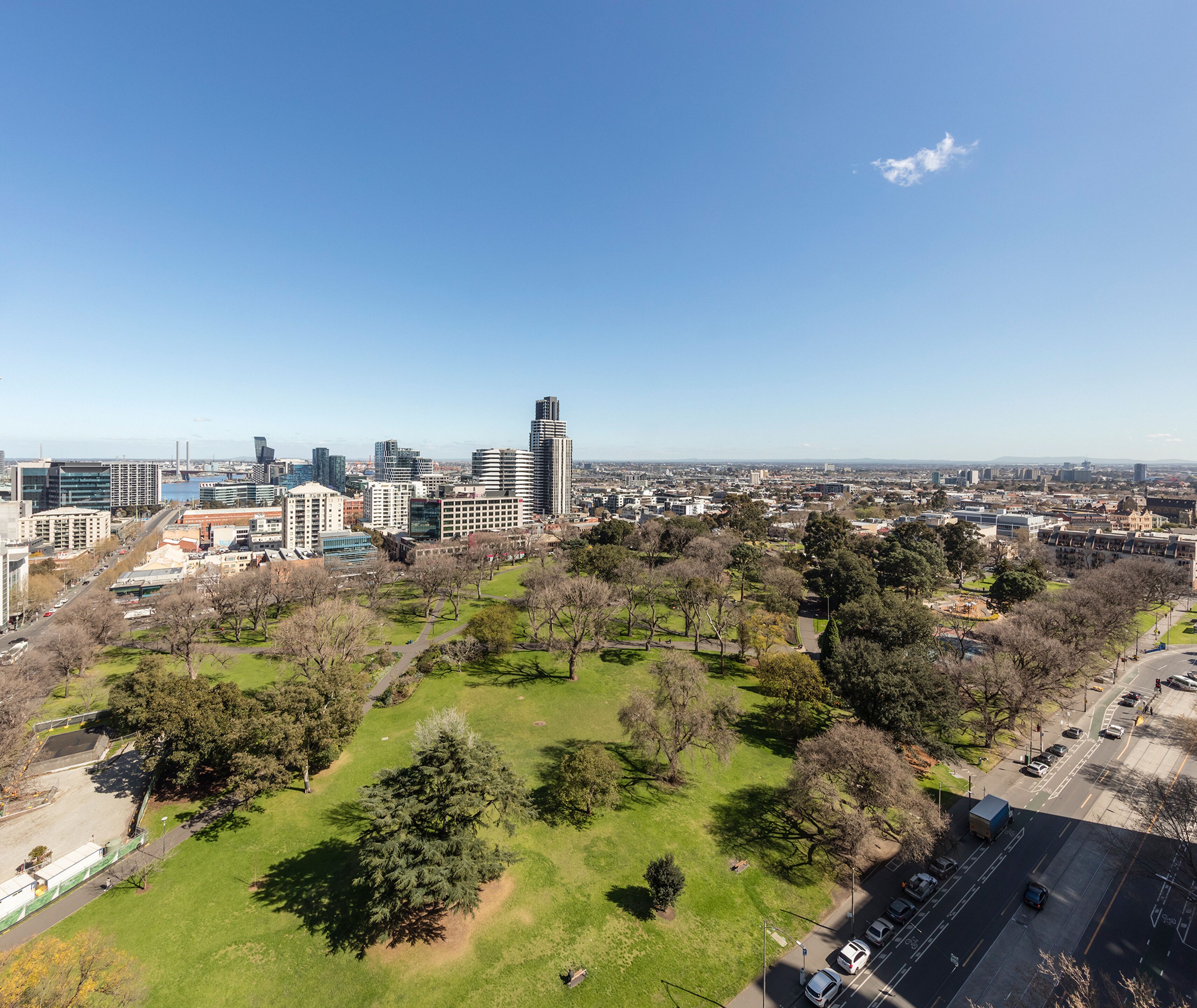 A cityscape with modern buildings, a park with trees, and a clear blue sky.