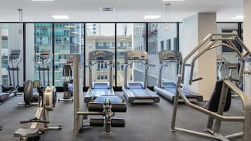 A gym with various exercise equipment, large windows, and a view of buildings.