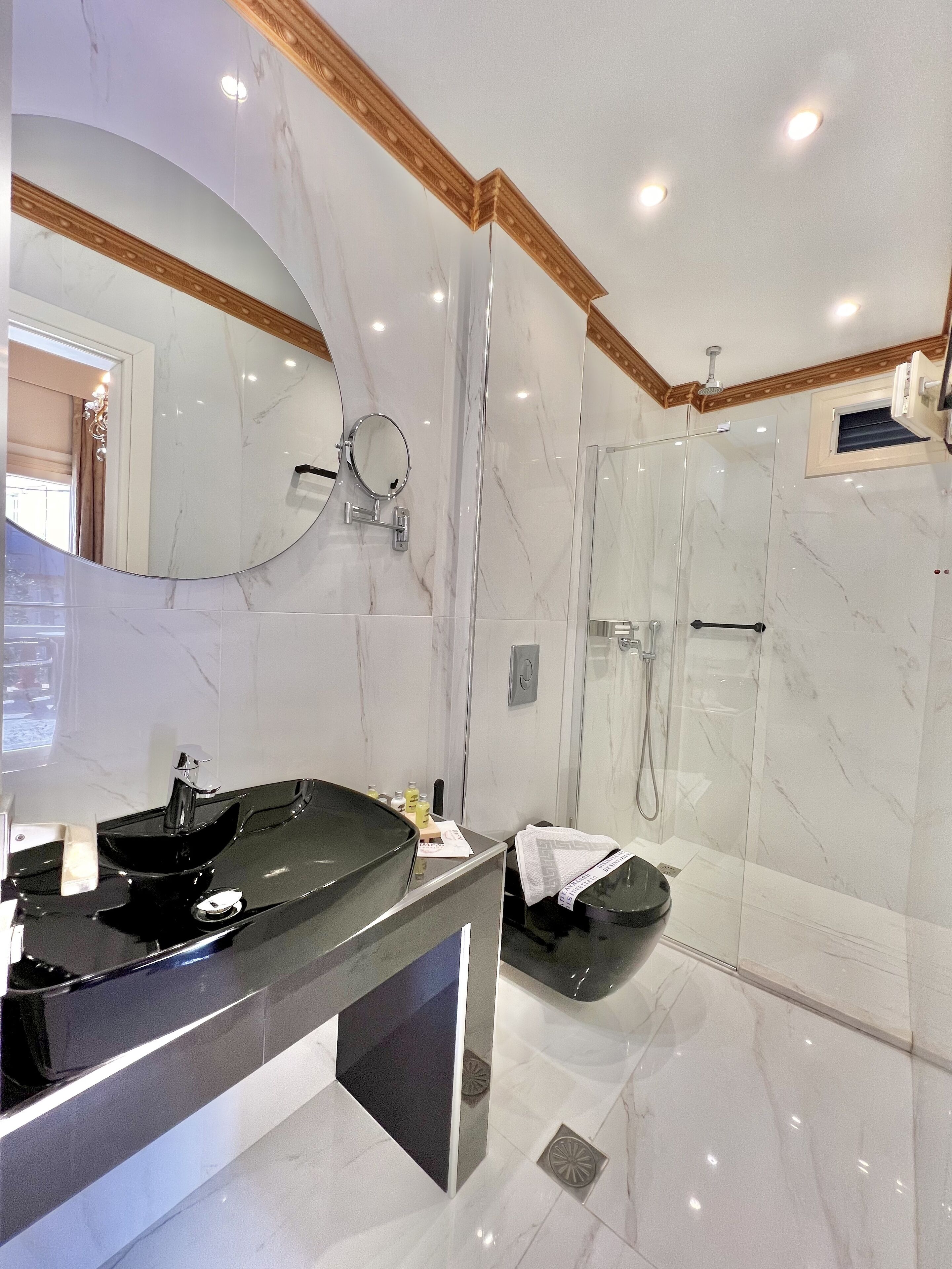 A modern bathroom with a marble vanity, a large mirror, a shower enclosure, and a ceiling with recessed lighting.