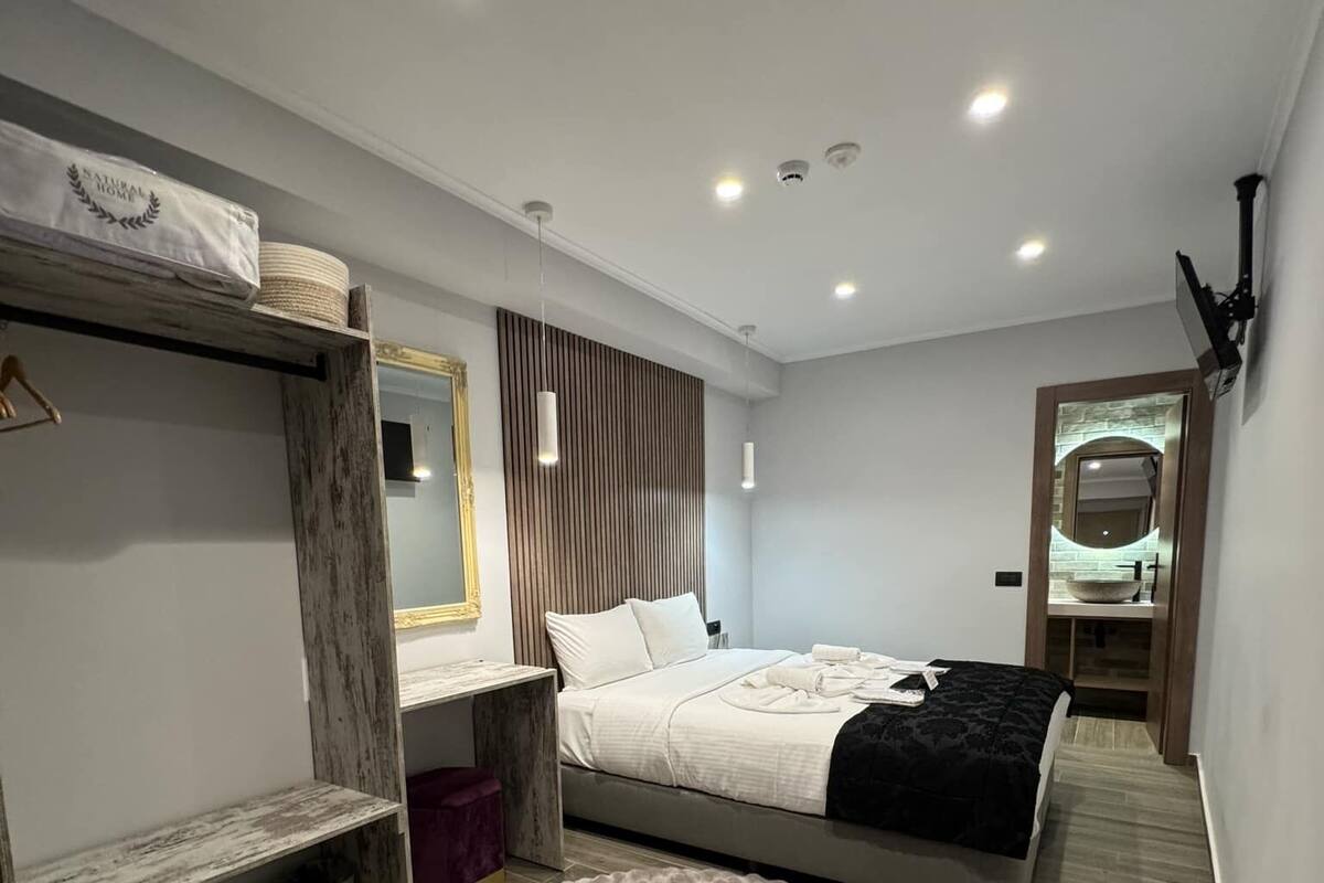 Un dormitorio moderno con una cama litera, un tapete redondo, una tocador con espejo, y un baño pequeño visible a través de una puerta.