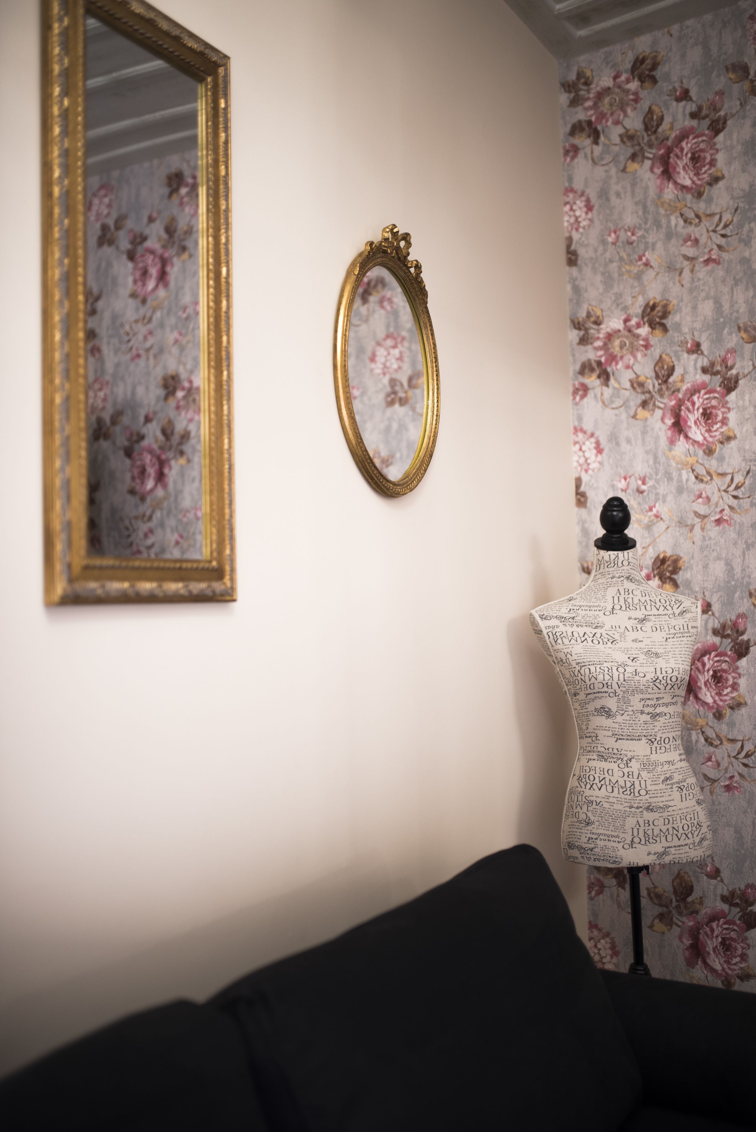 A room with a floral wallpaper, a gold-framed mirror, and a mannequin bust with a black top.