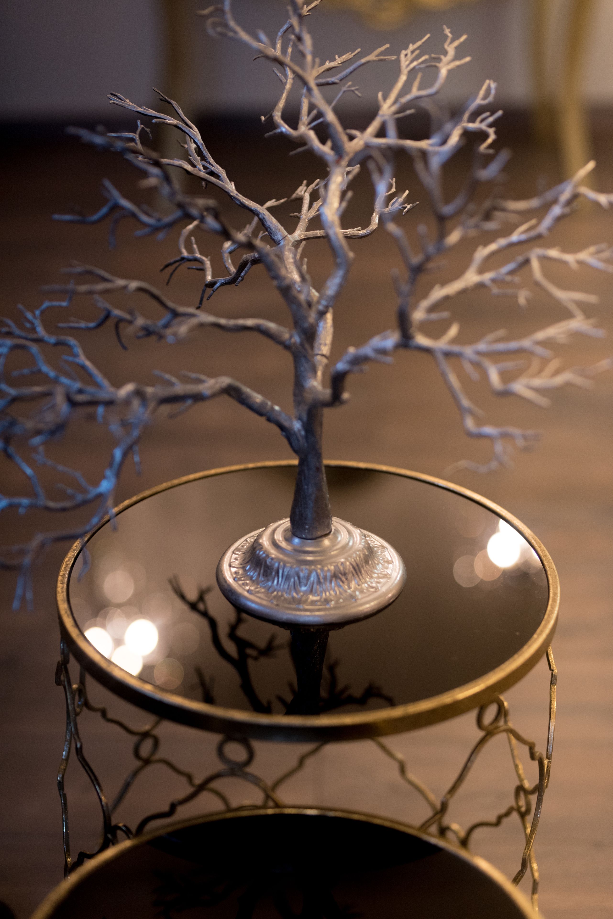 Une sculpture représentant un arbre, faite de métal, posée sur une table en verre réfléchissant.