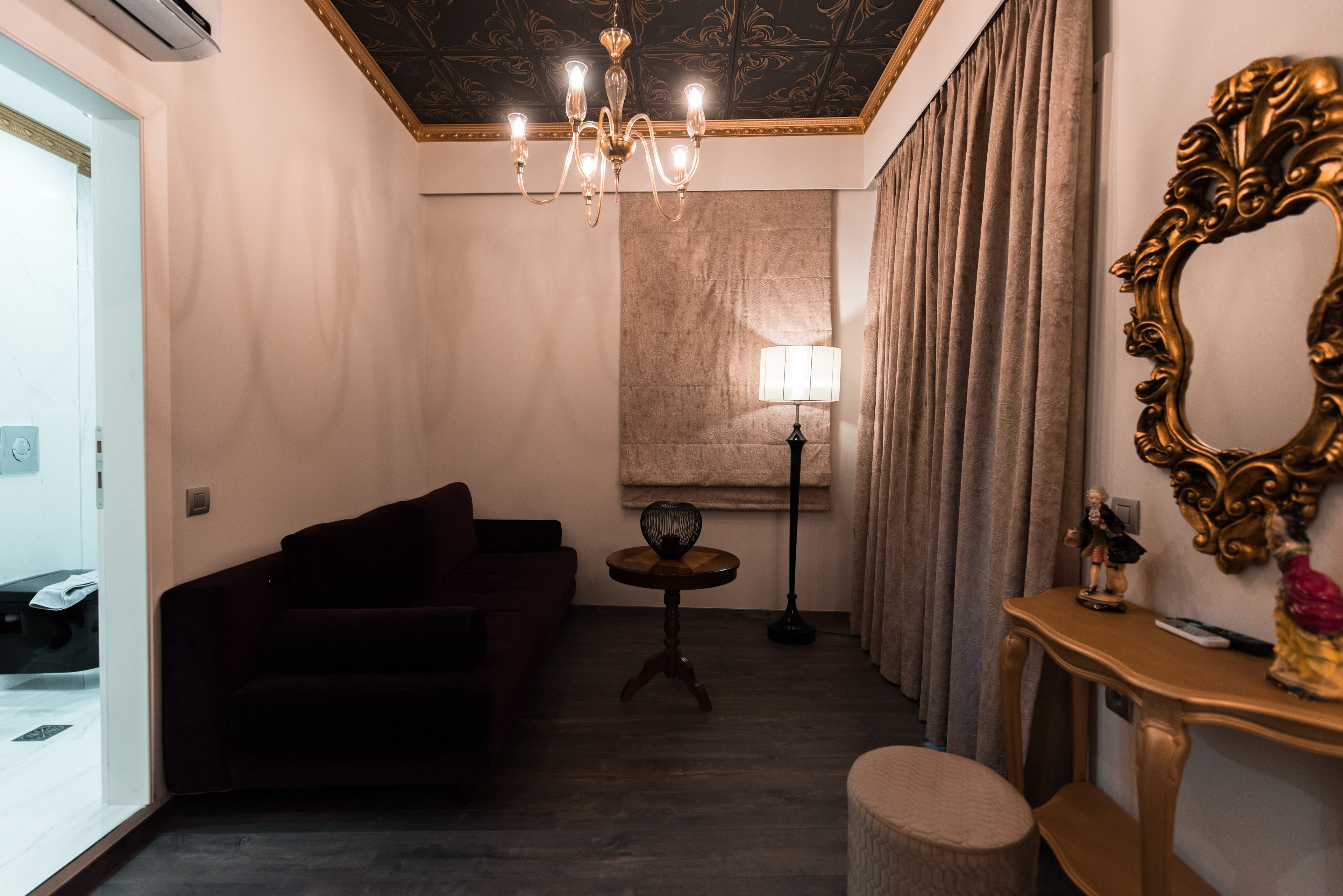 Una sala de estar con un sofá de color oscuro, una mesita redonda con una lámpara, un candelabro y un espejo grande sobre una consola de madera.