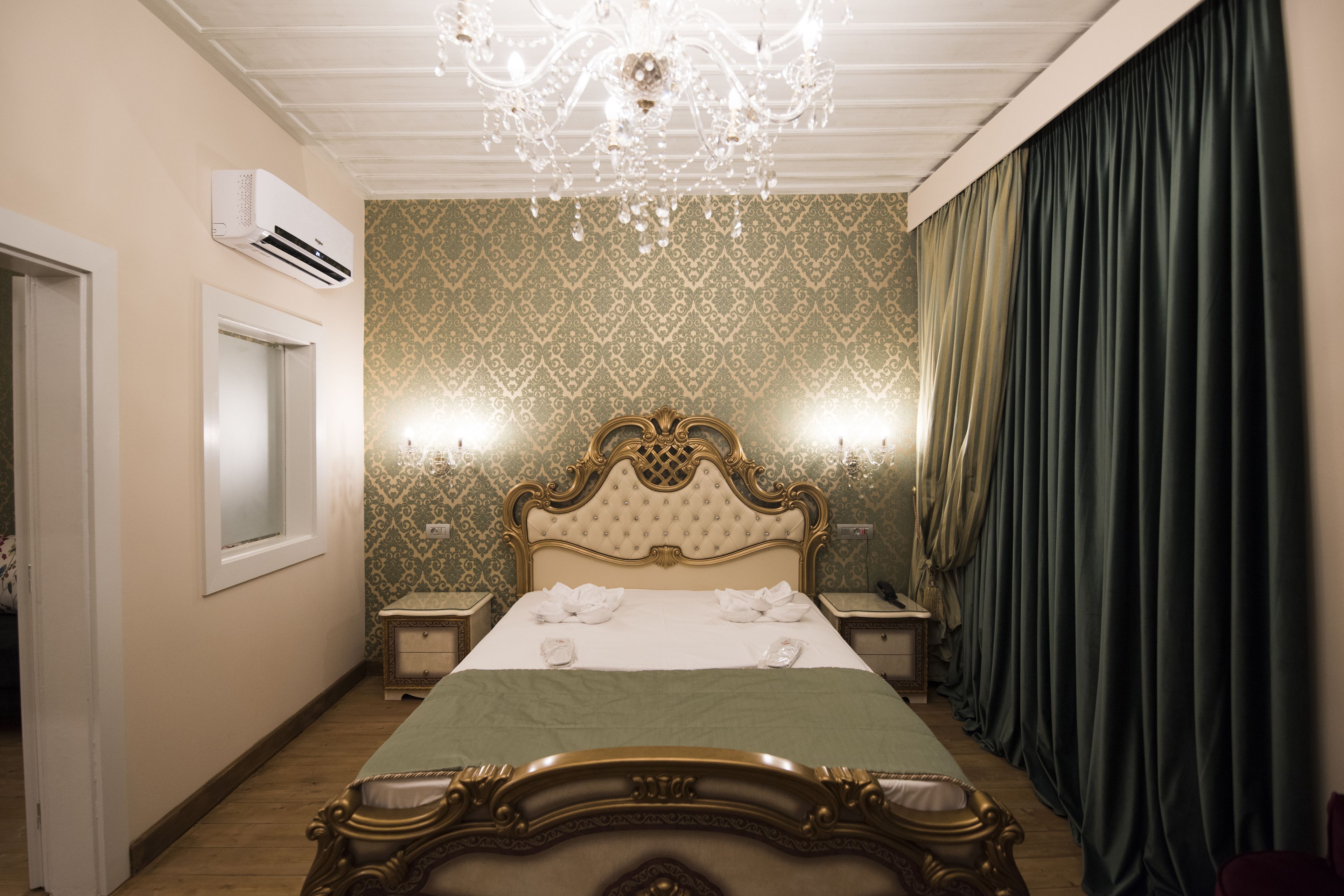 Une chambre d’hôtel avec un grand lit, un lustre, un climatiseur fixé au mur et une fenêtre avec des rideaux.