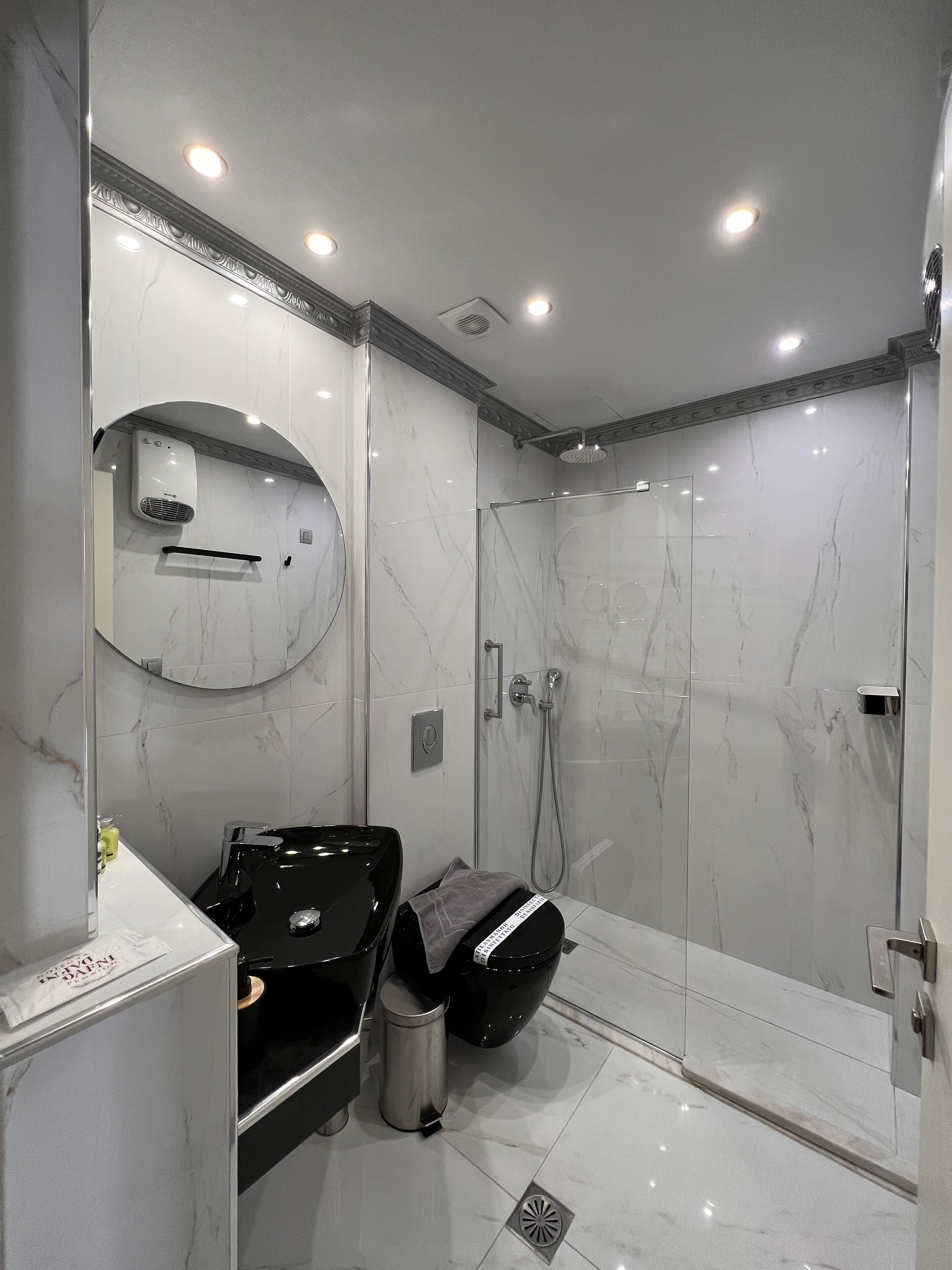 A modern bathroom with a glass-enclosed shower, a black sink, and a marble-tiled wall.