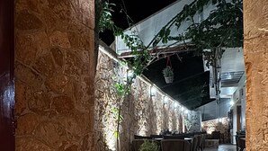 A stone-walled outdoor patio with tables and chairs, illuminated by ambient lighting. - Pension Dafni (Nafplio)