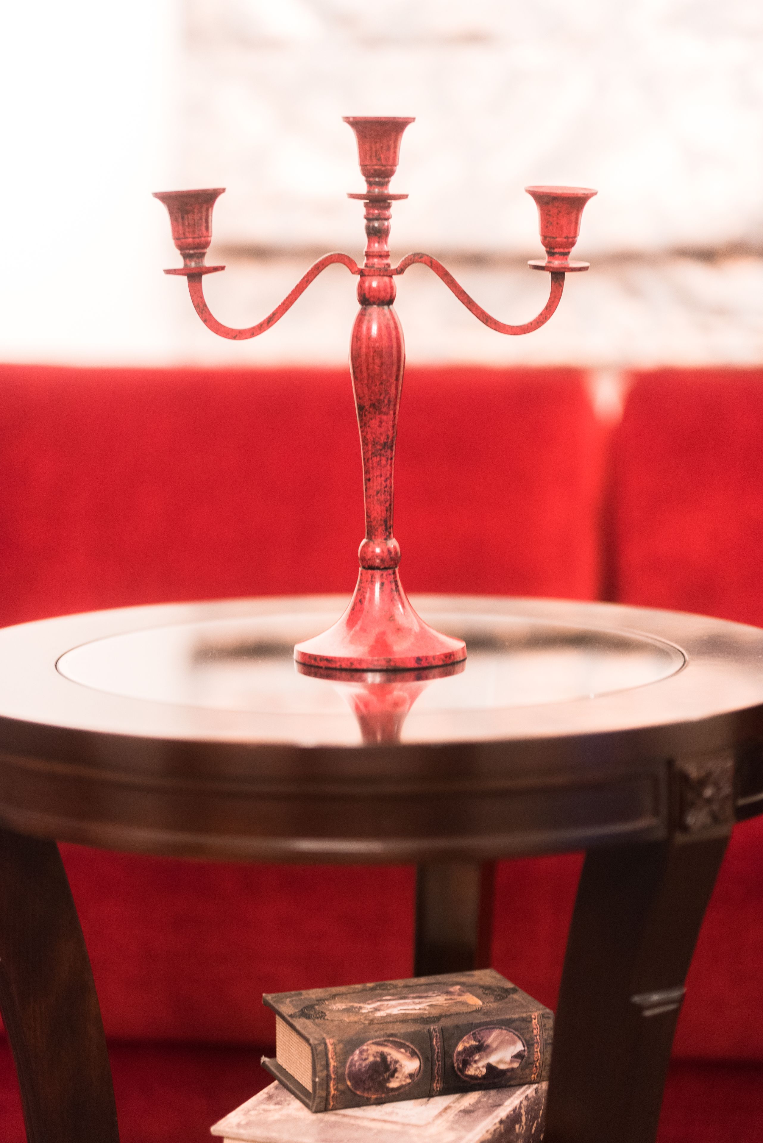 Un candelabro sobre una mesa redonda con un sofá tapizado en rojo al fondo.