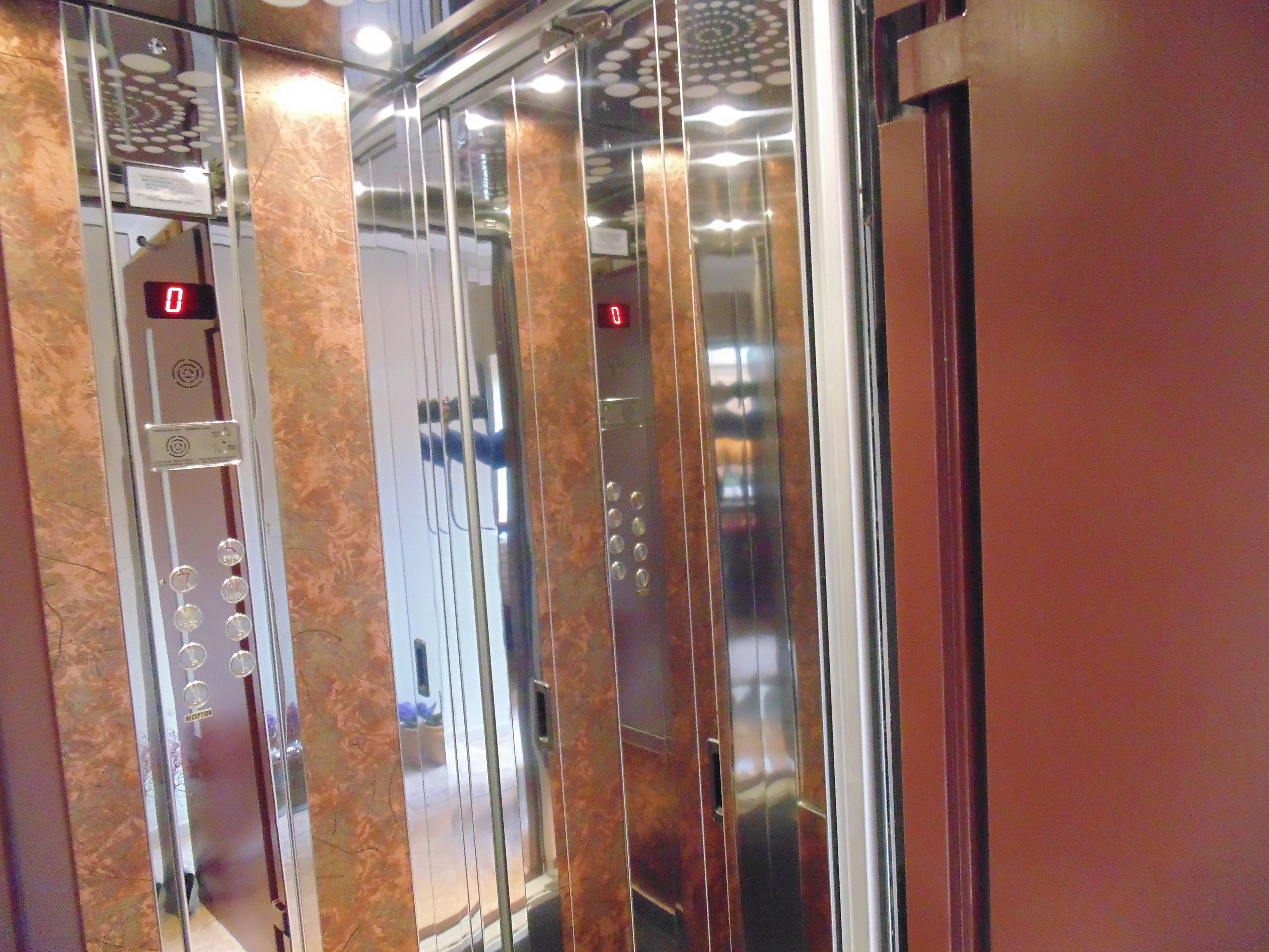 An elevator interior with a digital display, metallic walls, and a marble-like floor.
