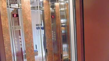 An elevator interior with a digital display, metallic walls, and a marble-like floor.