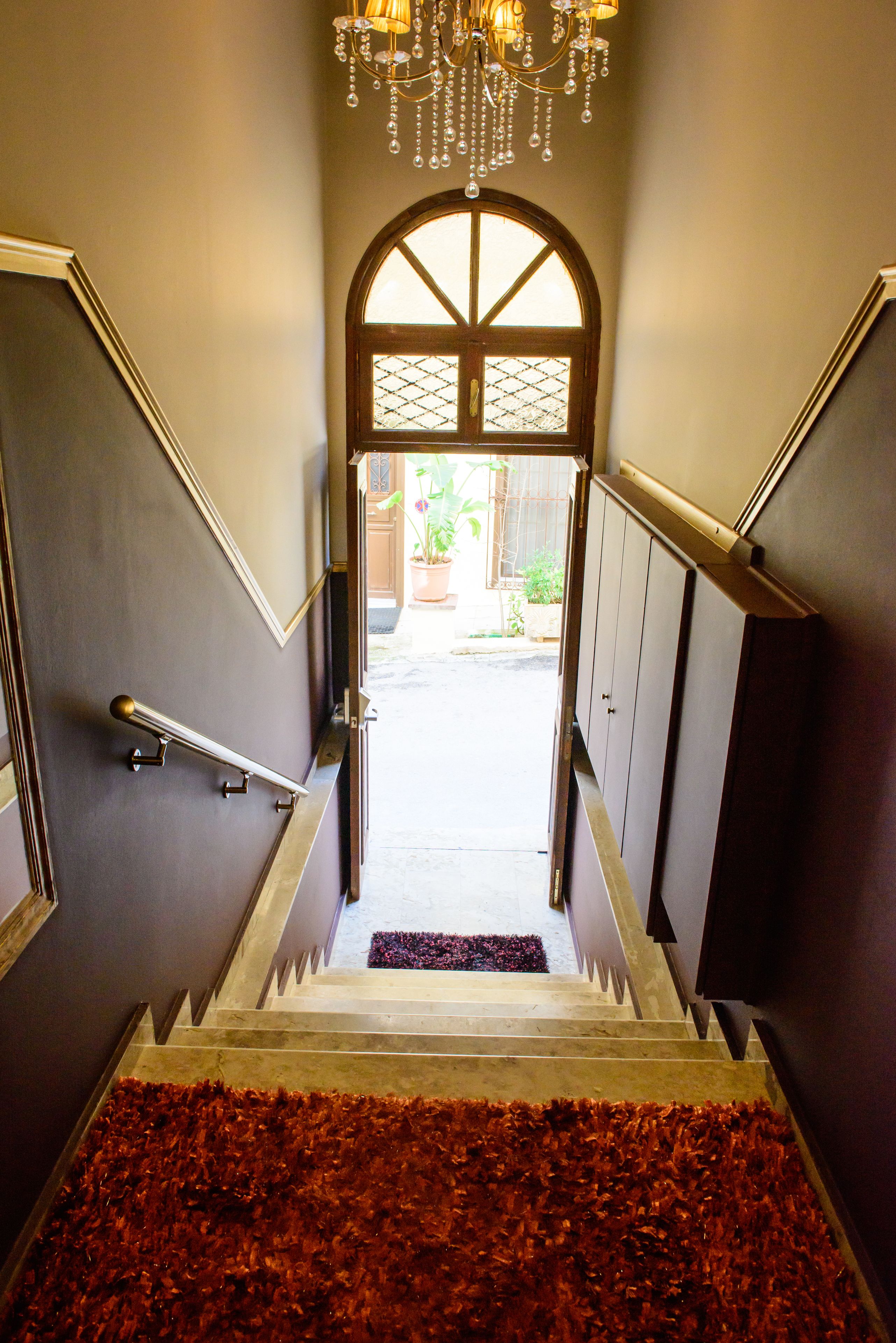A staircase with a handrail, a chandelier, and a view into a courtyard.