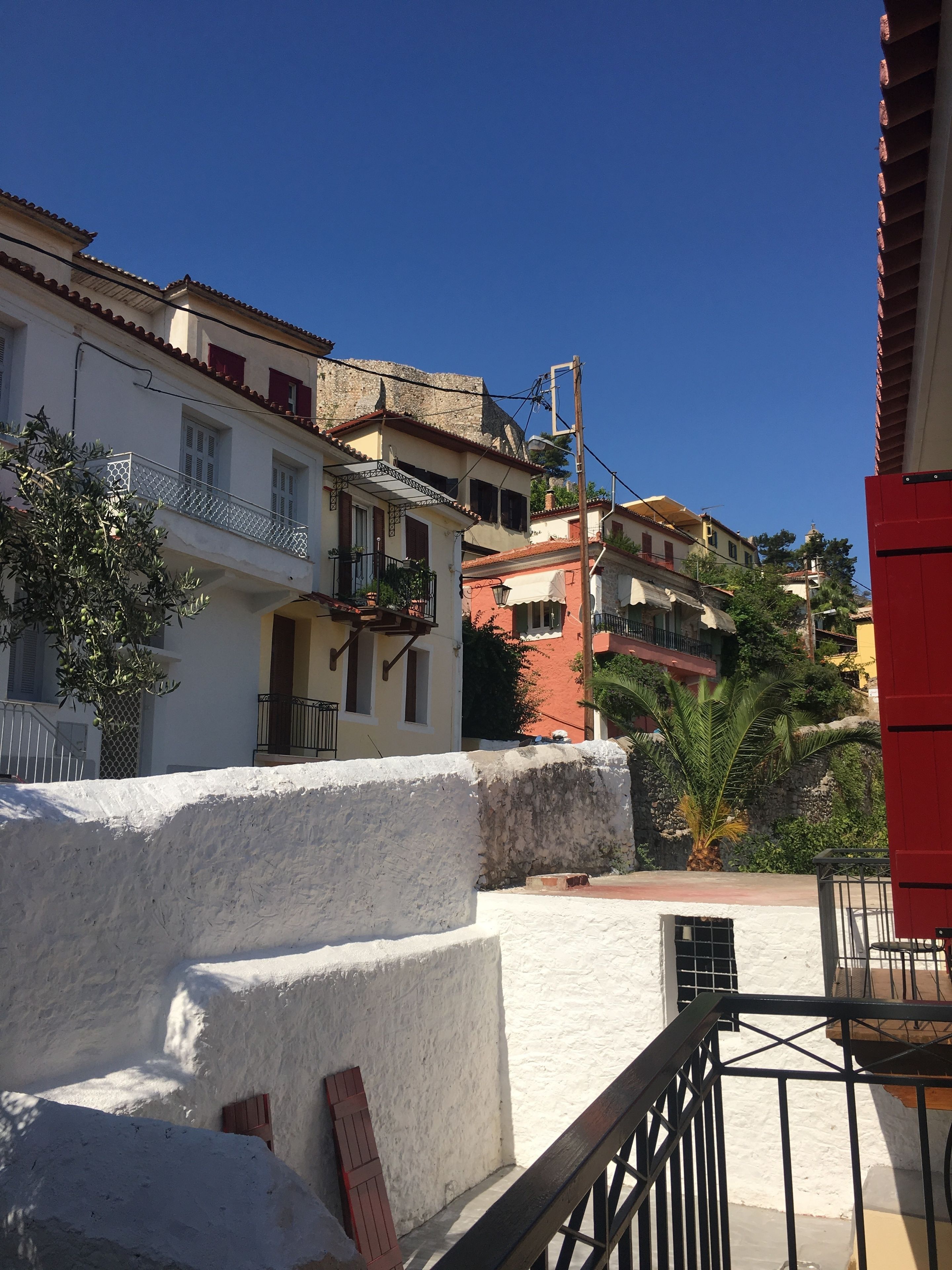 A coastal building with balconies, a white wall, and a red building in the background.