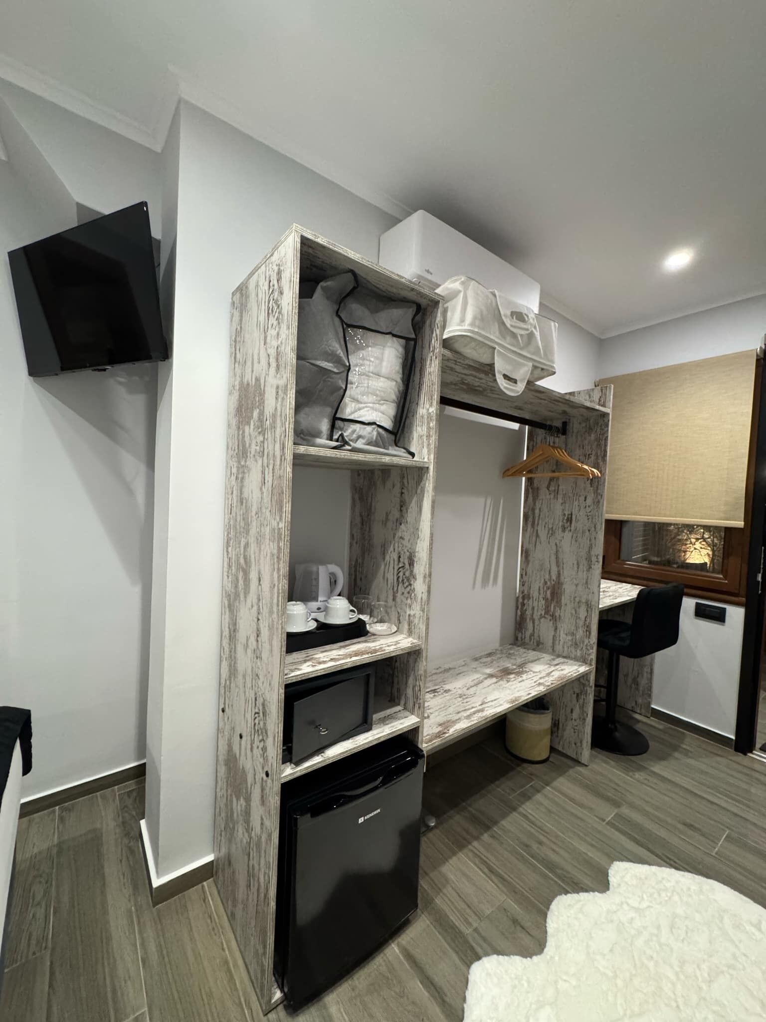 A compact living space with a built-in wardrobe, a small kitchenette, a seating area, and a television mounted on the wall.