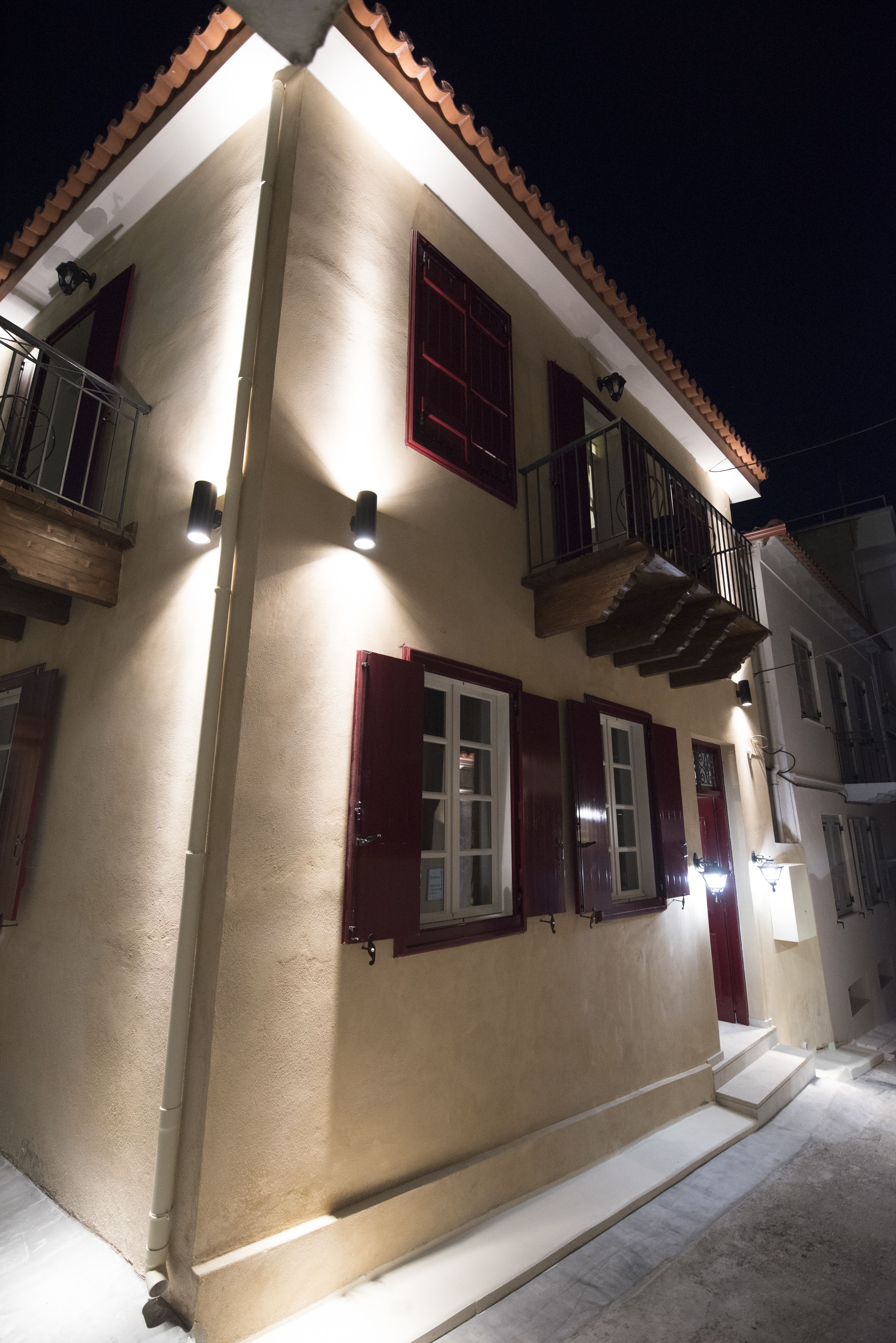 A two-story building with a beige facade, red shutters, and a balcony with a wooden railing.