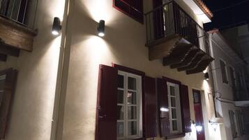 A two-story building with a beige facade, red shutters, and a balcony with a wooden railing.