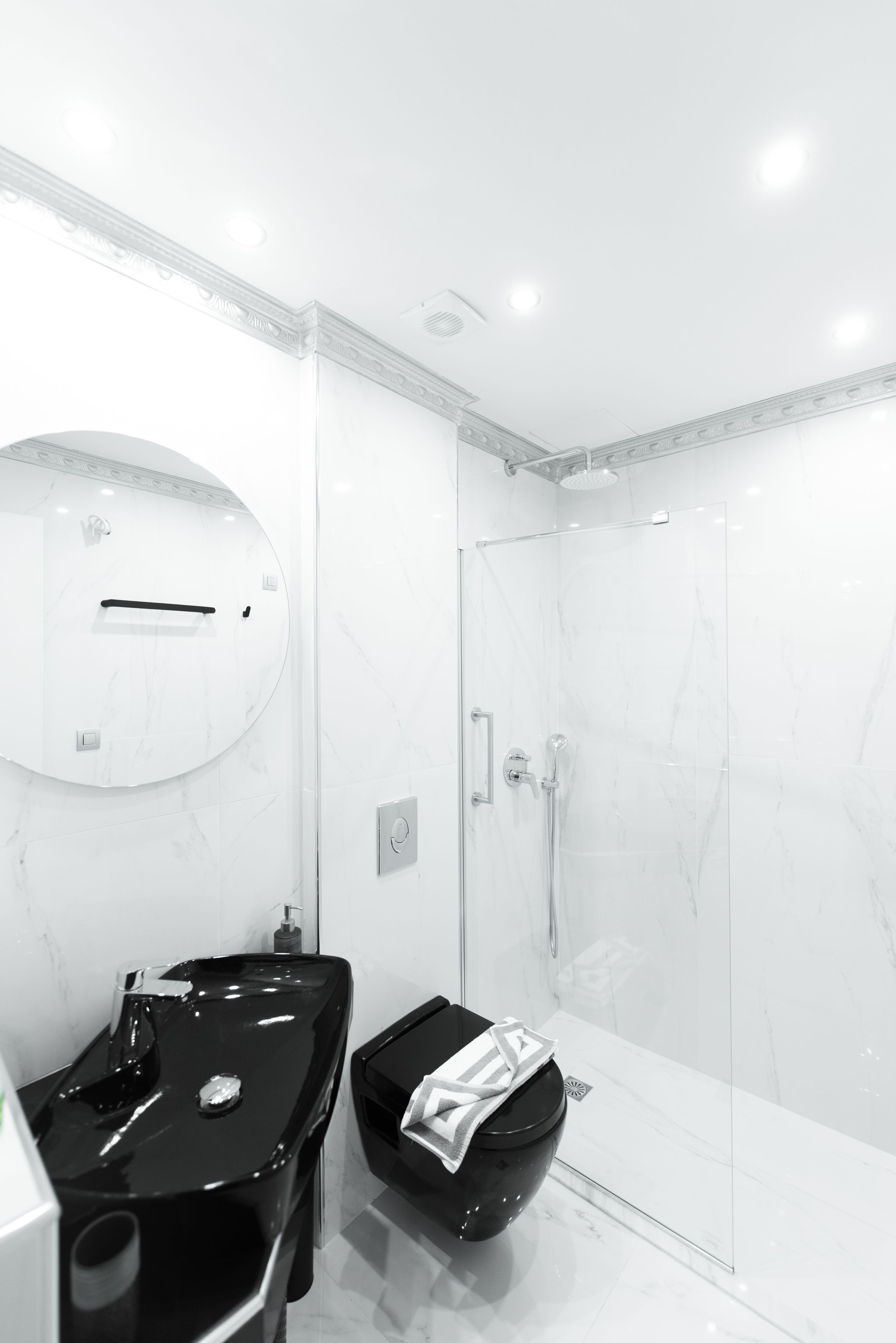 A modern bathroom with a glass shower enclosure, a black sink, and a marble-topped vanity.