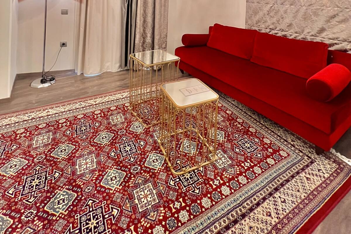 Un salón con sofá rojo, alfombra estampada y candelabro.