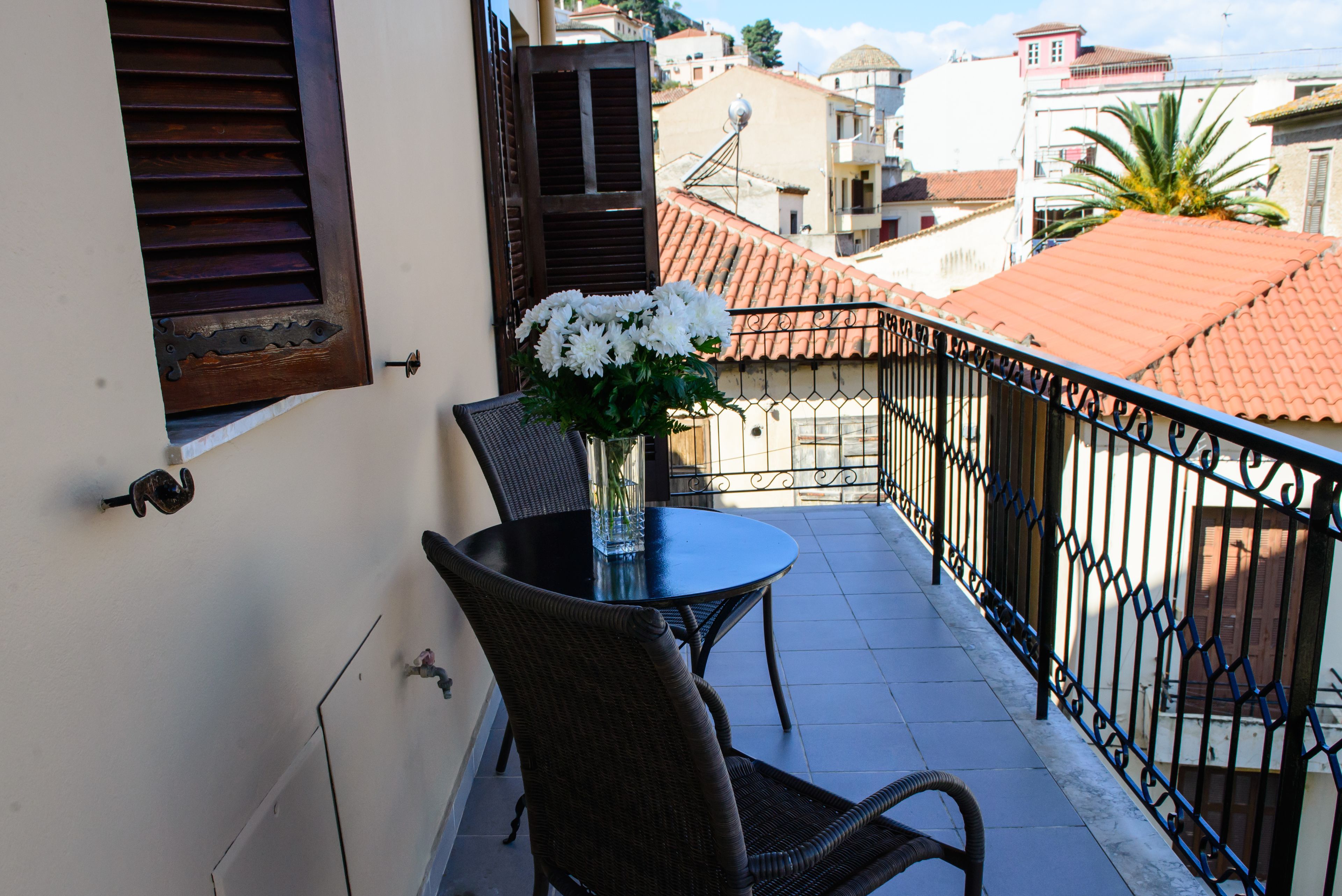 A balcony with a table and chairs, a vase with flowers, and a view of the surrounding buildings.