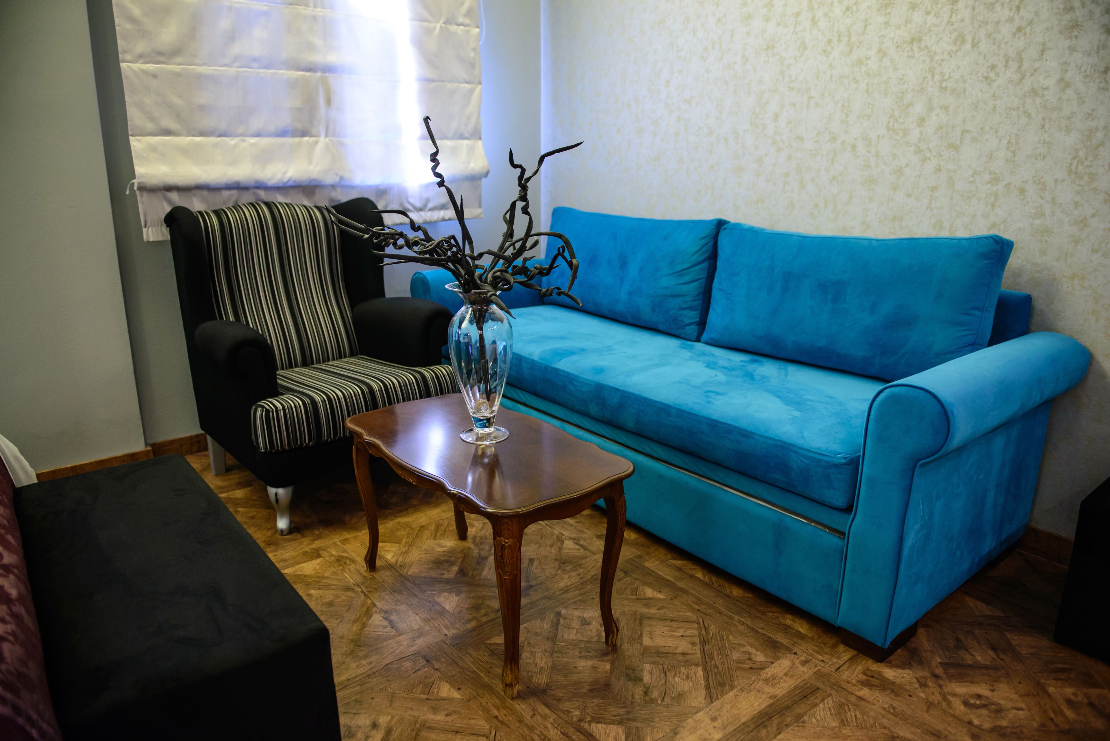 A living room with a blue sofa, a striped armchair, a wooden coffee table, and a vase with branches.