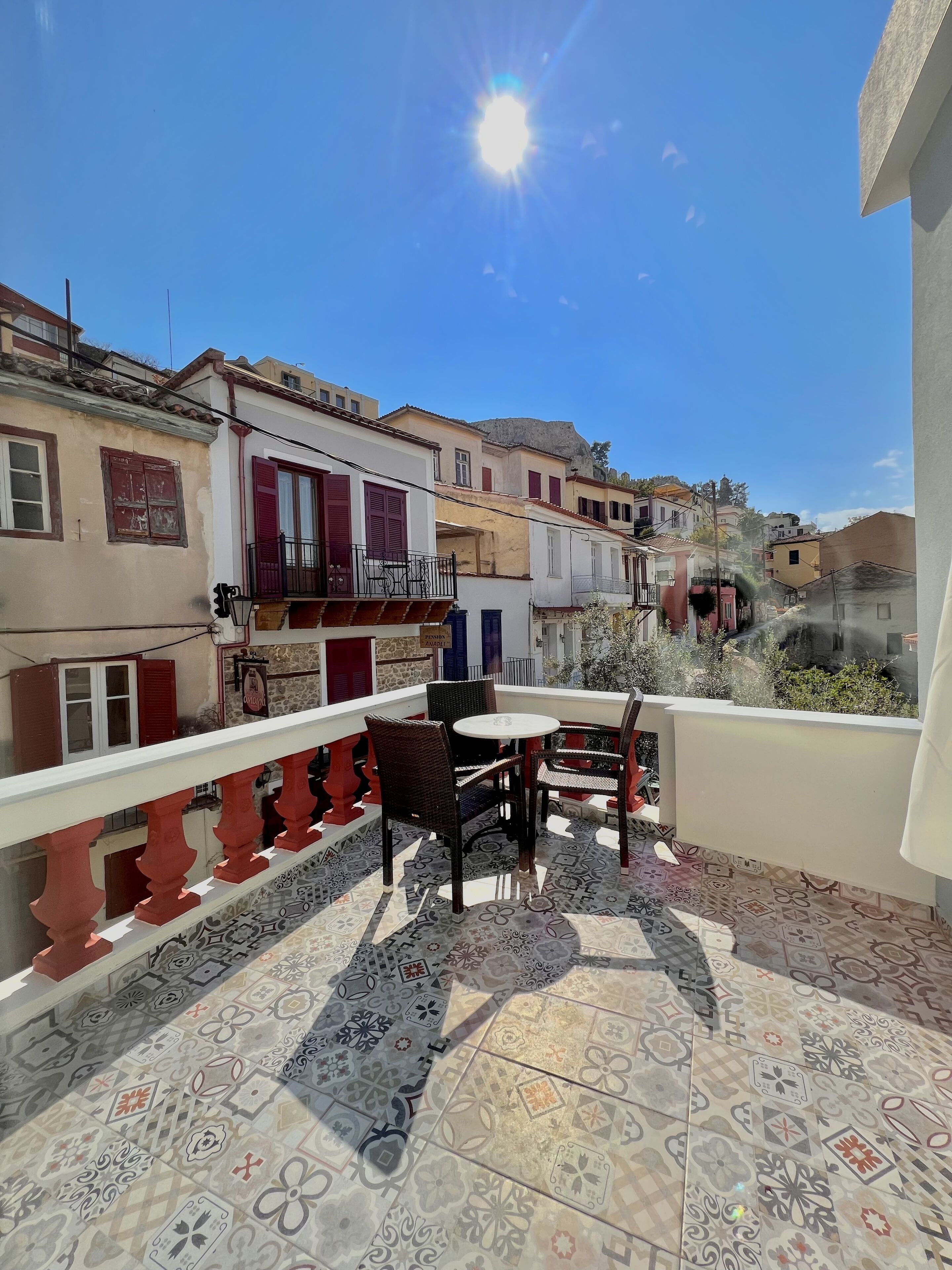 A terrace with patterned tiles, a table with chairs, and a view of neighboring buildings.
