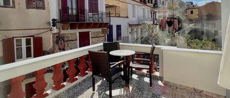 A terrace with patterned tiles, a table with chairs, and a view of neighboring buildings.