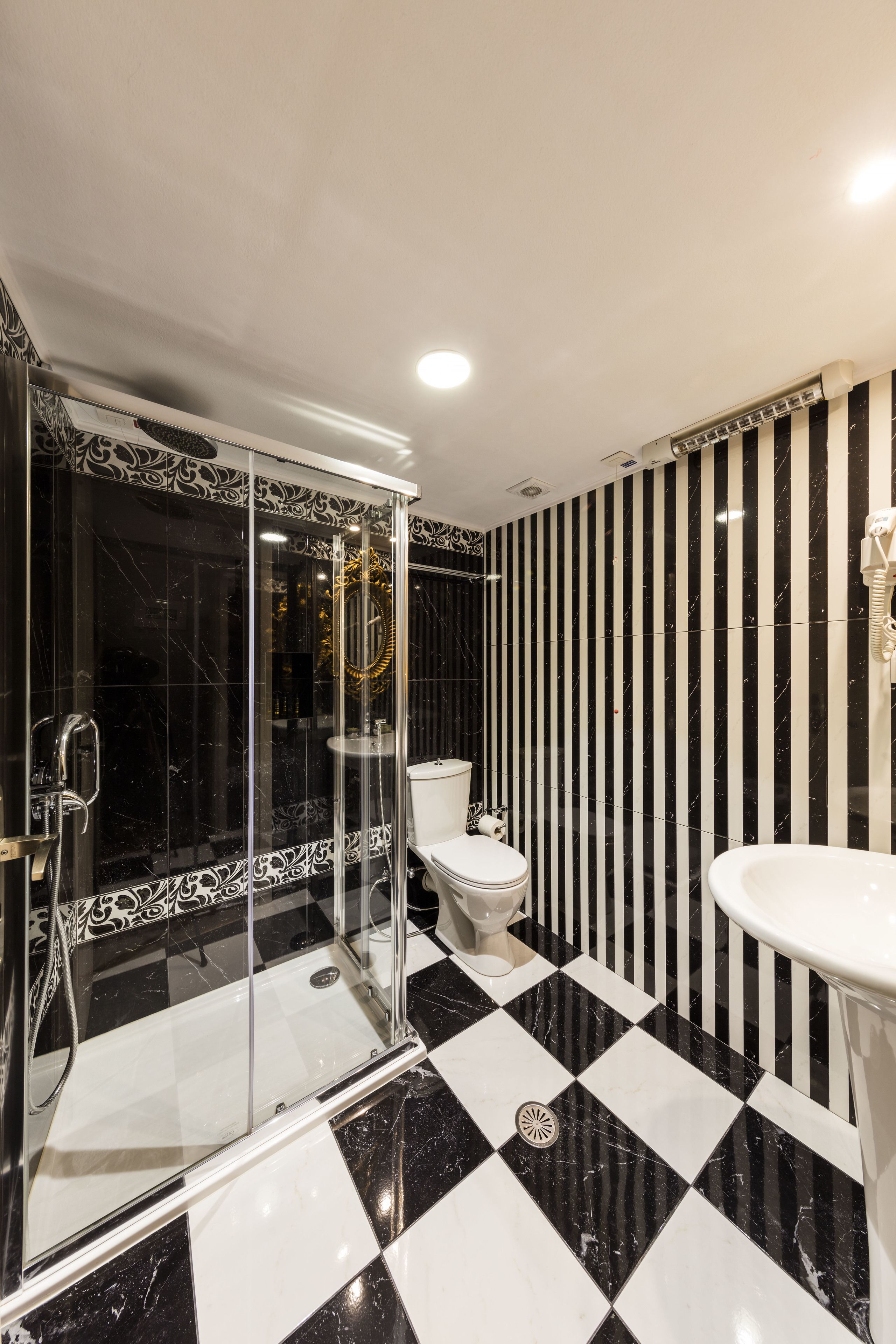 Un bany amb un terra negre i blanc a quadradets, un espai de banyera de vidre, un vàter i un lavabo.