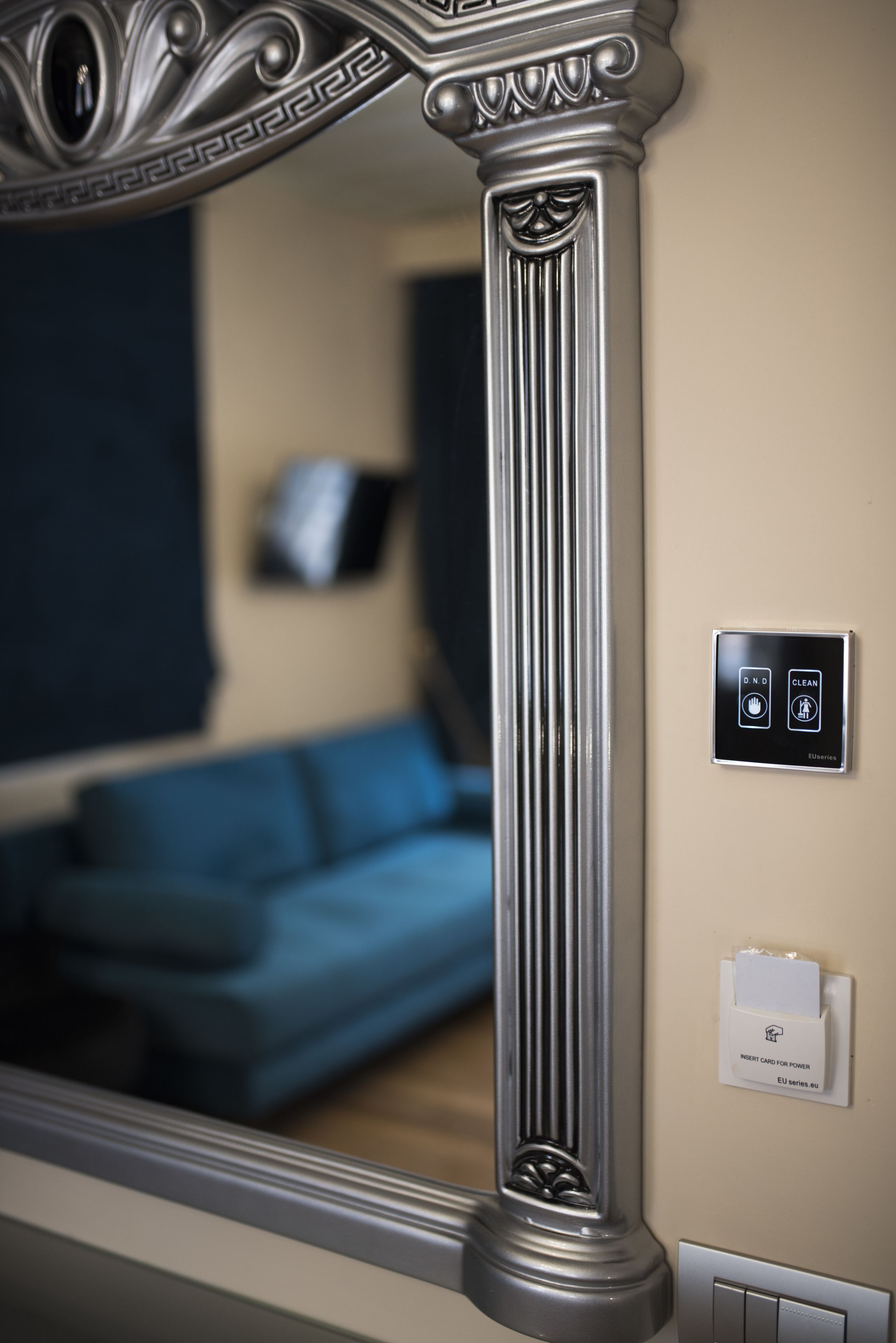 A mirror reflecting a room with a blue sofa, a wall-mounted TV, and a decorative column.